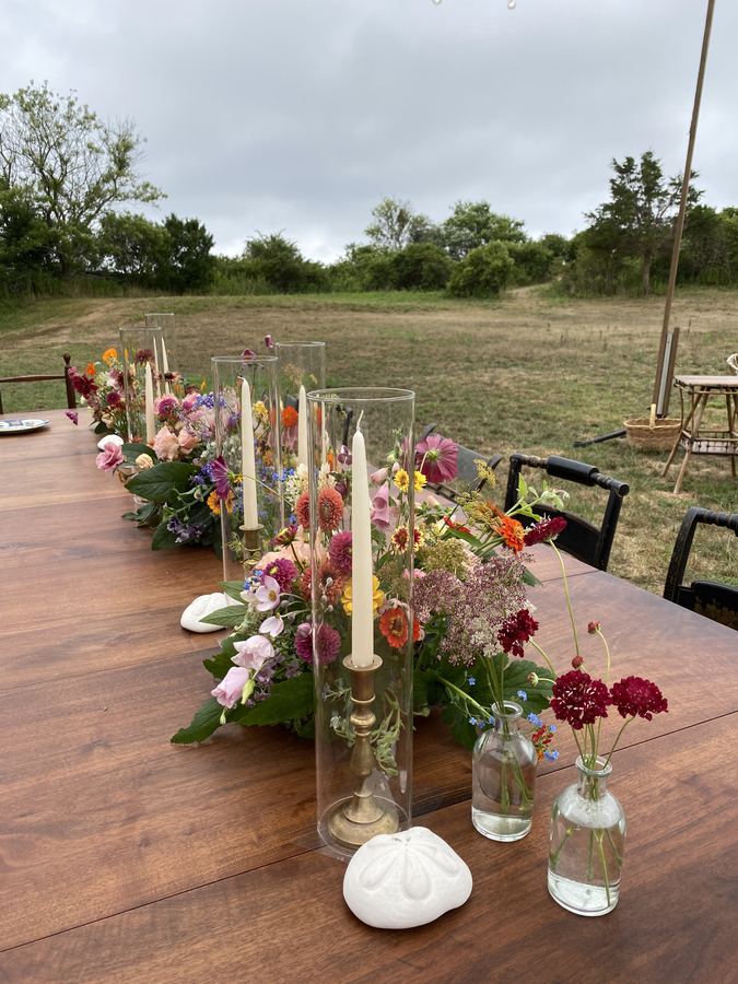 Outdoor table in a field, garden flowers in bottles, tapers